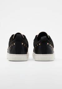 Svarta sneakers med överdel i mocka, med metalliska nitar och en texturerad läderhæl. Vit gummisula med en kontrasterande varumärkesetikett.