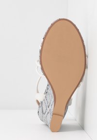 Chaussure à talons hauts avec un dessus en simili-cuir argenté texturé à motif serpent, des lacets blancs et une semelle en caoutchouc lisse couleur tan.