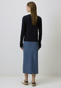 Marineblauwe trui van gebreide stof, gecombineerd met een lichtblauwe denimrok met een achtersplit. Het model draagt beige platform sneakers.