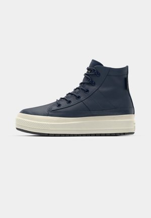 Zapatillas altas de cuero en color azul marino con una superficie texturizada, que cuentan con una suela de goma blanca y detalles en patrón negro en la suela exterior.