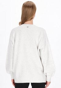 Przesadnie duży biały sweter o miękkiej fakturze, z małymi kolorowymi plamkami, z prążkowanymi ściągaczami i umiarkowanym dekoltem w łódkę.