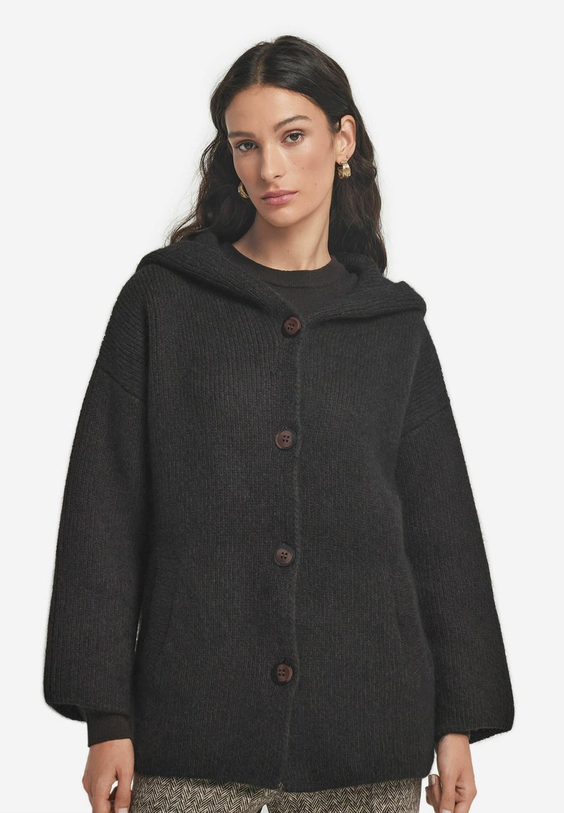 Mörkgrå huva cardigan gjord av texturerad stickad tyg, med en framknäppning, sidofickor och vida ärmar.