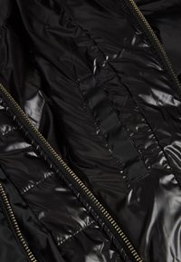 Wnętrze czarnej, pikowanej kurtki z błyszczącego nylonu, widoczne szwy i złote akcenty zamka błyskawicznego. Zawiera ukrytą kieszeń.