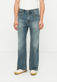 Lichtblauwe denim jeans met een relaxte pasvorm, voorzien van een rechte pijpdesign, subtiele vervaging en contrasterende stiksels. Gecombineerd met witte sneakers.