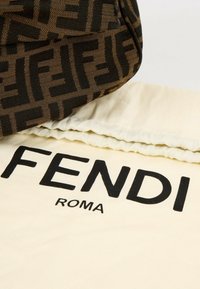 Tissu marron Fendi avec motif FF noir reposant sur un tissu crème imprimé FENDI ROMA en lettres noires épaisses.