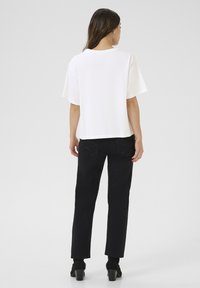 T-shirt blanc à manches courtes et col rond associé à un pantalon noir taille haute et des bottines. Le pantalon comporte des poches arrière distinctives.