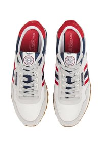 Sneaker retrò con tomaia in canvas color crema, caratterizzate da strisce rosse e blu navy. Suola in gomma, punta rotonda e dettagli con marchio sulla linguetta.
