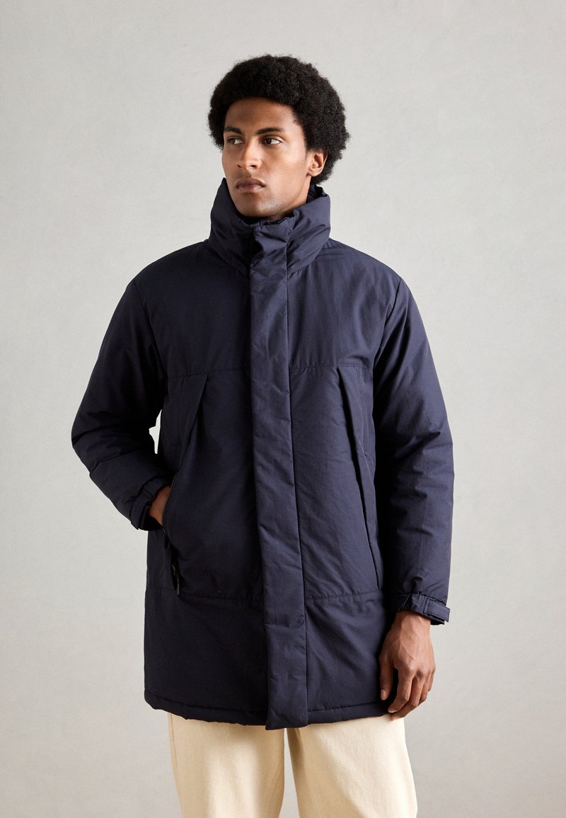 Casaco acolchoado azul-marinho com gola alta, fecho frontal por zíper e bolsos laterais. Fabricado em um tecido suave com um corte descontraído.