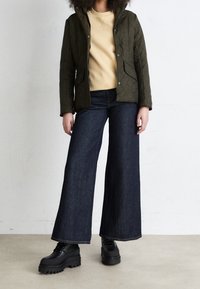 Quilted olive green jacket with a hood, beige sweater, wide-leg dark denim jeans, and black platform boots. Textured fabric, casual fit.