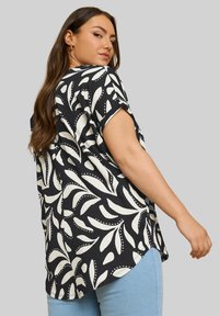 Camicia a maniche corte a righe bianco e nero, con un motivo a foglia e tessuto testurizzato, abbinata a jeans blu.