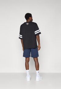 Fekete, túlméretezett póló fehér csíkokkal az ujjain, logóval a hátsó részen, sötétkék sorttal és fehér sportcipőkkel párosítva. Az anyag simának tűnik.