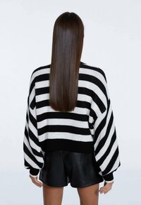 Maglione oversize a righe bianche e nere con spalle scese e polsini a coste, abbinato a pantaloni di pelle neri.