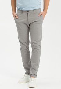 Szare spodnie z bawełny, dopasowane, z subtelnym wzorem w kratkę, standardowymi kieszeniami i zapięciem na guzik. Noszone z białymi trampkami.
