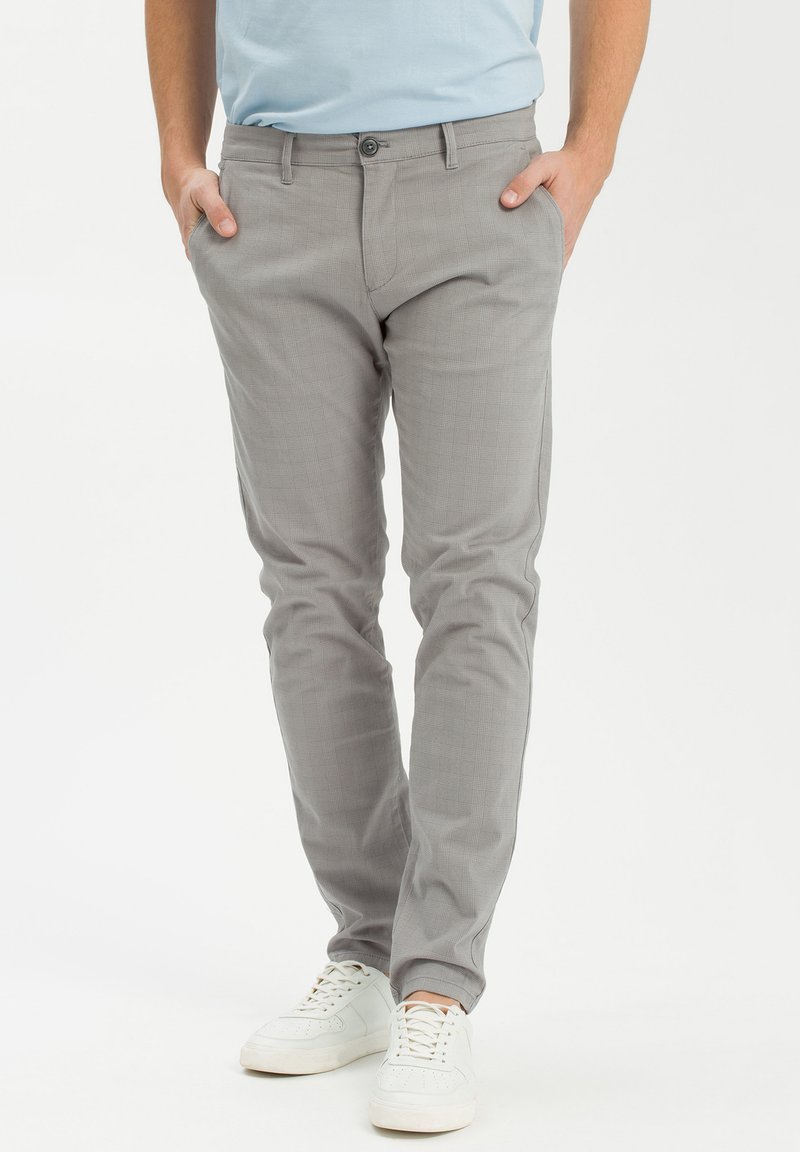 Szare spodnie z bawełny, dopasowane, z subtelnym wzorem w kratkę, standardowymi kieszeniami i zapięciem na guzik. Noszone z białymi trampkami.