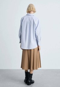 Blue and white striped button-up shirt with long sleeves, paired with a beige pleated skirt and black ankle boots.