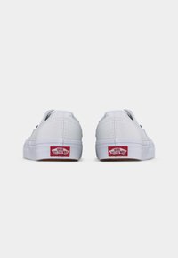 Paire de baskets Vans blanches vues de dos, avec le logo rouge "Vans Off The Wall" sur les semelles en caoutchouc blanches.