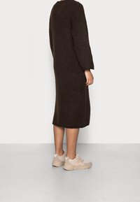 Braunes gestricktes Midikleid mit langen Ärmeln, kombiniert mit hellbeigen Sneakern, die über strukturierte Akzente und eine glatte Sohle verfügen.