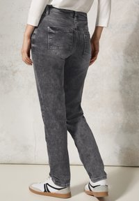 Jeans in denim grigio con una vestibilità comoda, dotati di un alta vita, cinque tasche e una finitura sbiadita. Abbinati a scarpe da ginnastica bianche e grigie.