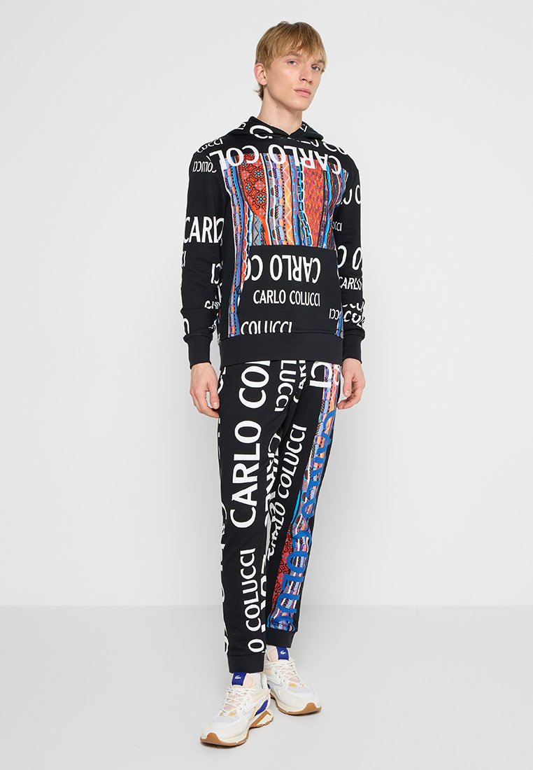 Conjunto de sudadera con capucha negra y pantalones de chándal con patrones gráficos coloridos y texto grande. Fabricado con un tejido suave y con puños de canalé.