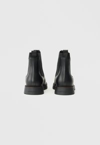 Stivali alla caviglia in pelle nera con pannelli elastici laterali, finitura liscia, punta tonda e suola in gomma. Design minimalista con un dettaglio di branding sottile.