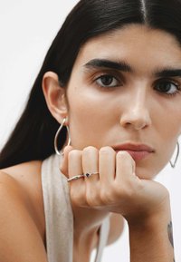 Anillo de plata con una piedra preciosa azul, con un diseño delicado. Pendientes grandes de aro de plata y una blusa texturada de color claro.