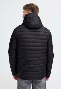 Sort puffjakke med hætte, der har en quiltet design, letvægtsmateriale og en lige pasform. Synlige sømme og teksturdetaillering.