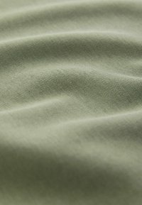 Nahaufnahme eines glatten, hellgrünen Stoffes mit sanften Falten und sichtbar feiner Textur.