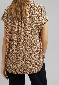 Blusa a fantasia floreale in beige, bordeaux e giallo, con maniche corte e vestibilità ampia. Presenta un dettaglio plissettato sul retro.