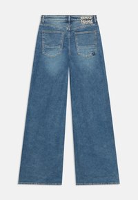 Blaue weit geschnittene Jeans aus Denim, mit hoher Taille, zwei Gesäßtaschen und einem Etikett im Leopardenmuster. Glatte Textur.