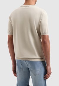 Beige korte mouwen trui met een geribbelde ronde hals, een gestructureerde stof en een relaxte pasvorm, gecombineerd met lichtblauwe spijkerbroek.