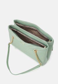 Zelená prošívaná kabelka z texturovaného syntetického materiálu se zlatými řetízkovými detaily, obsahující dvě kapsy na zip a ramenní popruh.