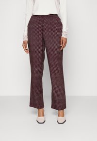 Calças largas em tecido texturizado burgundy com um padrão geométrico, apresentando uma cintura elástica e combinadas com saltos de cor clara.