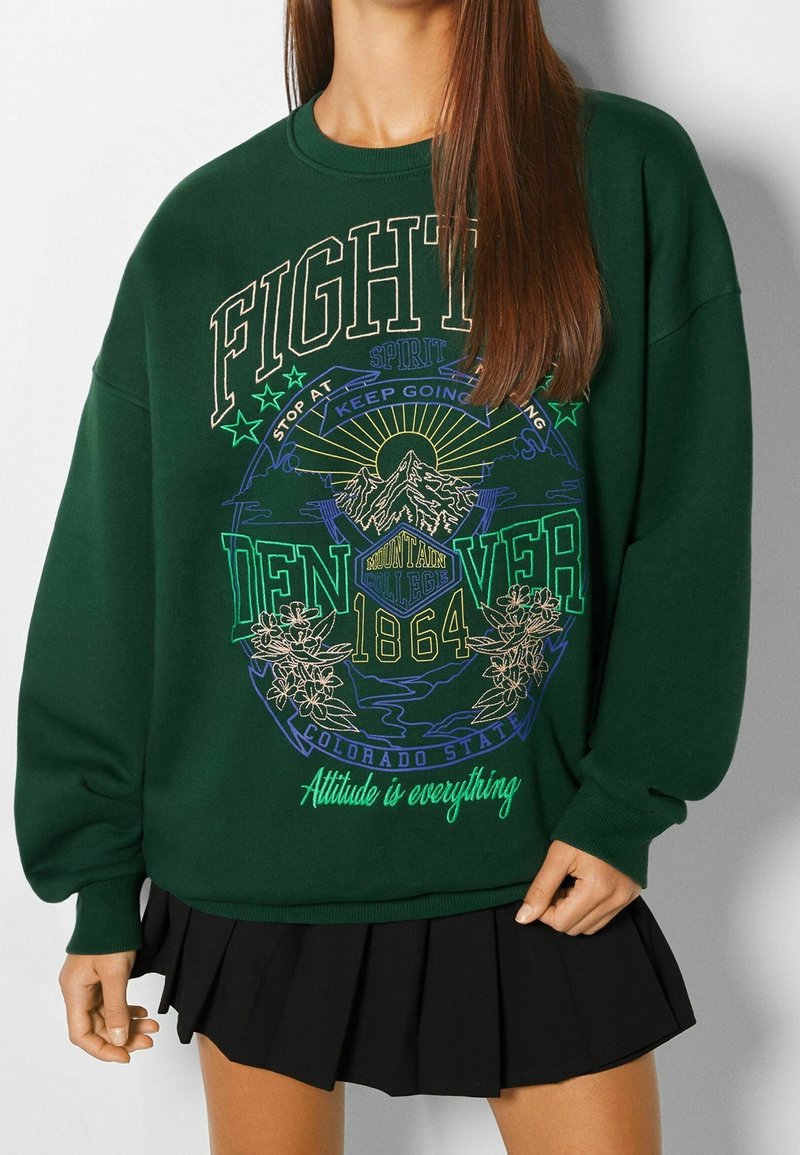 Grön sweatshirt med grafisk design som visar "Denver" och bergmotiv, tillsammans med en svart veckad kjol. Tillverkad av bomull, avslappnad passform.