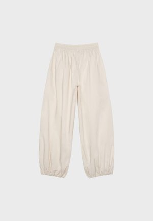 Pantalon ample de couleur crème avec taille élastique et poignets élastiques froncés, présenté à plat sur un fond neutre.