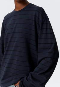 Μπλε ναυτικό μακρυμάνικο T-shirt από βαμβάκι, με οριζόντιες μαύρες ρίγες, στρογγυλή λαιμόκοψη και χαλαρή εφαρμογή με ραμμένα στους ώμους.