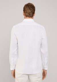 Chemise en lin blanc à manches longues avec un col classique, dotée de poignets boutonnés et d'un ourlet arrondi. Texture lisse avec un aspect léger et aérien.