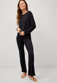 Sort ribbet loungewear sæt, der indeholder en langærmet top og brede bukser. Blød tekstur og afslappet pasform designet til komfort.
