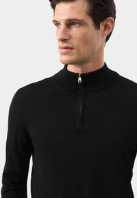 Černý svetr na zip s vroubkovaným límcem, vyrobený z měkkého materiálu. Má krátký zip na krku a přiléhavé dlouhé rukávy.