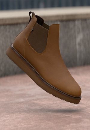 Brown leather ankle boot with elastic side panels, smooth texture, rounded toe, and a contrasting brown rubber sole. No visible hardware.