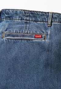 Poche arrière d'un jean en denim bleu avec une petite étiquette rouge de la marque Levi's cousue près du coin supérieur droit de la poche.
