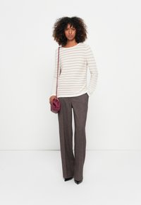 Gestreifter beiger und weißer Pullover kombiniert mit braunen strukturierten weit geschnittenen Hosen. Accessoires: eine kleine burgunderfarbene Handtasche und schwarze High Heels.