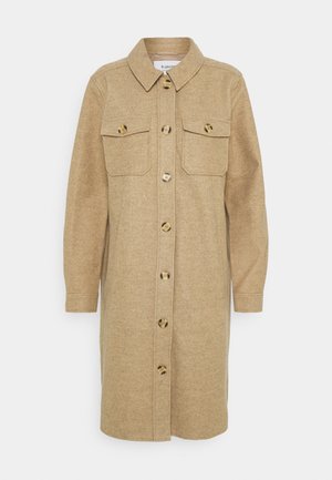 Beige wollen overhemdjurk met een kraag, lange mouwen, knoopsluiting aan de voorkant en twee borstzakken met ronde knopen.