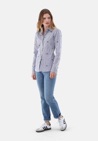 Striped button-up shirt with small floral embroidery, paired with light blue jeans and white sneakers featuring black stripes.