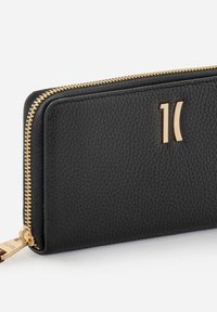 Czarny skórzany portfel o fakturowanej powierzchni, złote zamki błyskawiczne i tłoczone logo na przedzie. Prostokątny kształt o klasycznym wzornictwie.