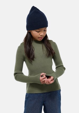 Pull à manches longues côtelé vert olive associé à un bonnet tricoté bleu foncé. Le pull présente un design ajusté avec des trous pour les pouces aux manches.