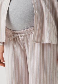 Ensemble de pyjama comprenant une chemise à boutons avec des rayures beige et blanches et un pantalon à cordon assorti avec une taille élastique.