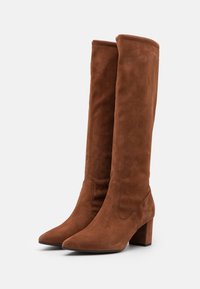 Bottes en suède marron montantes, à bout pointu et talon bloc. Texture lisse et design sans couture, sans matériel ou motifs visibles.