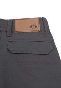 Gray fabric pants featuring a square pocket and a brown leather patch with embossed lettering. The texture is smooth with a checkered pattern.