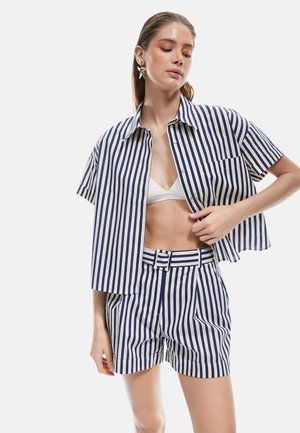 Chemise à rayures à manches courtes en bleu marine et blanc, associée à un short taille haute assorti. Présente une coupe droite et des boutons.