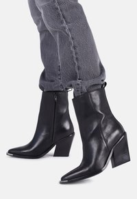 Czarne skórzane botki za kostkę z ostrym noskiem i wysokim blokowym obcasem. Posiadają boczny zamek błyskawiczny oraz gładką, błyszczącą fakturę.